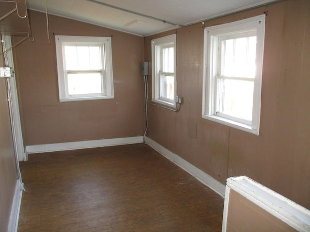 empty room with wood finished floors, baseboards, plenty of natural light, and vaulted ceiling