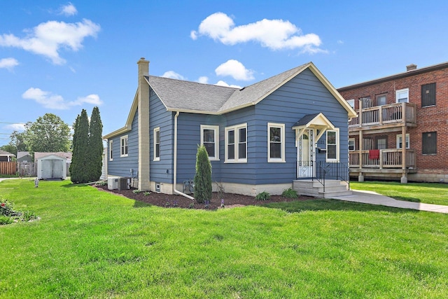 view of front of property with a chimney, a storage shed, roof with shingles, a front yard, and an outbuilding