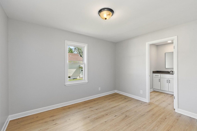 unfurnished room featuring light wood finished floors, baseboards, and a sink