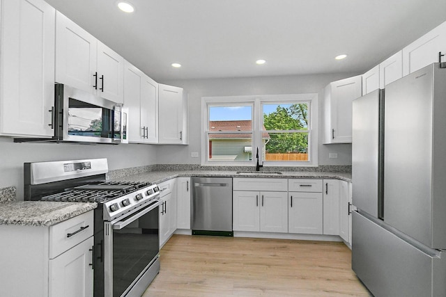 kitchen featuring appliances with stainless steel finishes, a sink, recessed lighting, white cabinets, and light wood-style flooring