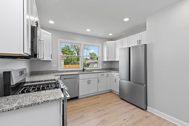 kitchen featuring stainless steel appliances, a sink, light stone counters, recessed lighting, and white cabinetry