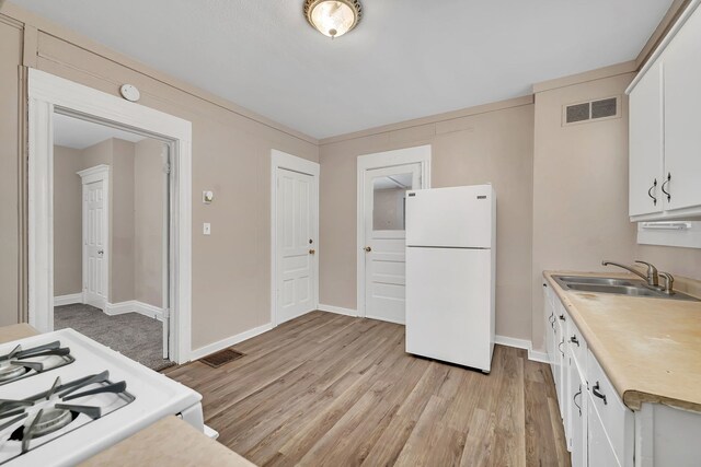kitchen featuring freestanding refrigerator, a sink, light wood finished floors, white cabinets, and light countertops