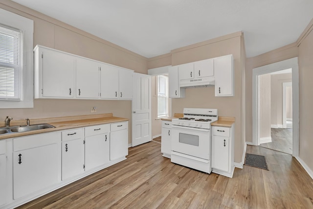 kitchen featuring gas range gas stove, a sink, light countertops, light wood-type flooring, and white cabinetry