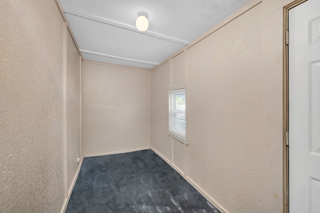empty room featuring a textured wall, dark colored carpet, and baseboards