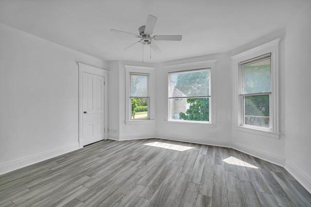 unfurnished room with wood finished floors, a ceiling fan, and baseboards