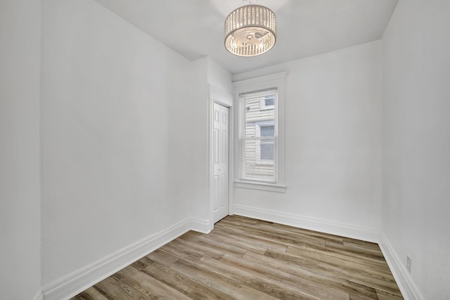 spare room with a chandelier, wood finished floors, and baseboards