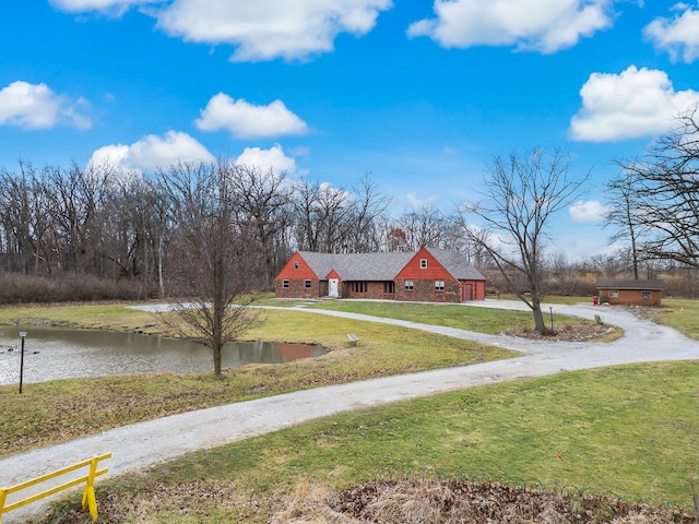 view of green lawn with driveway, a water view, and a garage