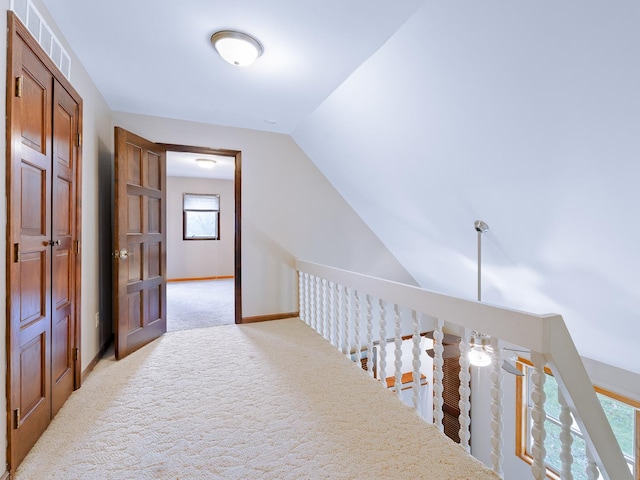 hallway featuring light carpet, lofted ceiling, and baseboards