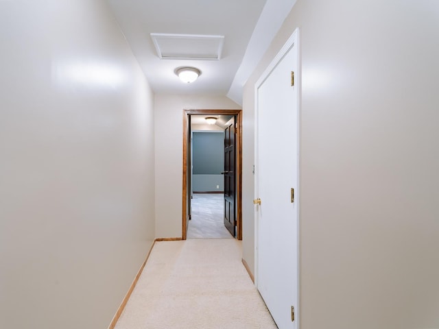 hallway with attic access, light colored carpet, vaulted ceiling, and baseboards