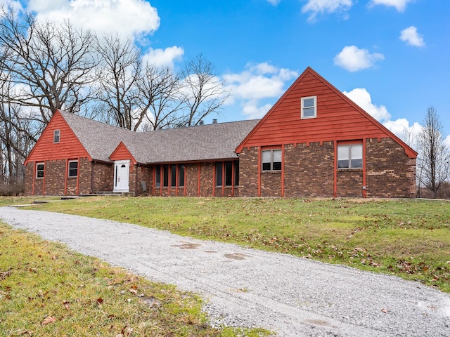 view of front facade with brick siding, a front lawn, and roof with shingles