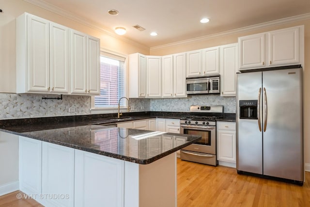 kitchen with stainless steel appliances, a peninsula, a sink, dark stone countertops, and light wood-style flooring