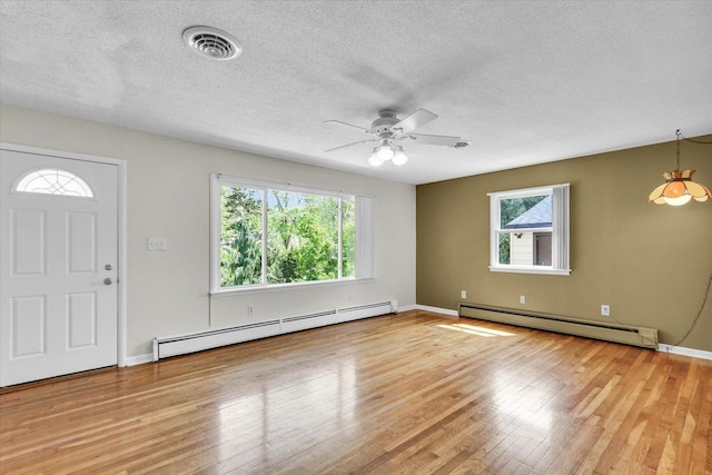 foyer entrance with a baseboard heating unit, healthy amount of natural light, light wood-style floors, and a textured ceiling