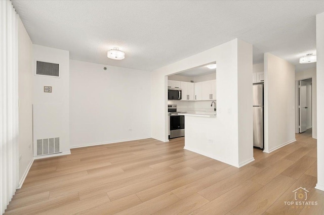 unfurnished living room featuring light wood-style flooring, a textured ceiling, baseboards, and a sink