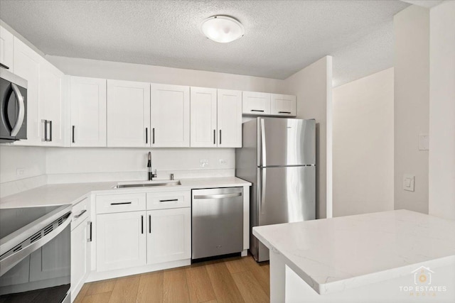 kitchen featuring stainless steel appliances, a sink, white cabinets, light wood finished floors, and a textured ceiling