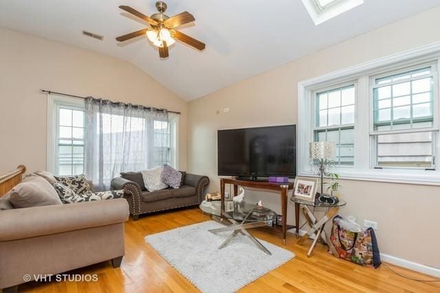 living area featuring healthy amount of natural light, lofted ceiling, wood finished floors, a ceiling fan, and a skylight