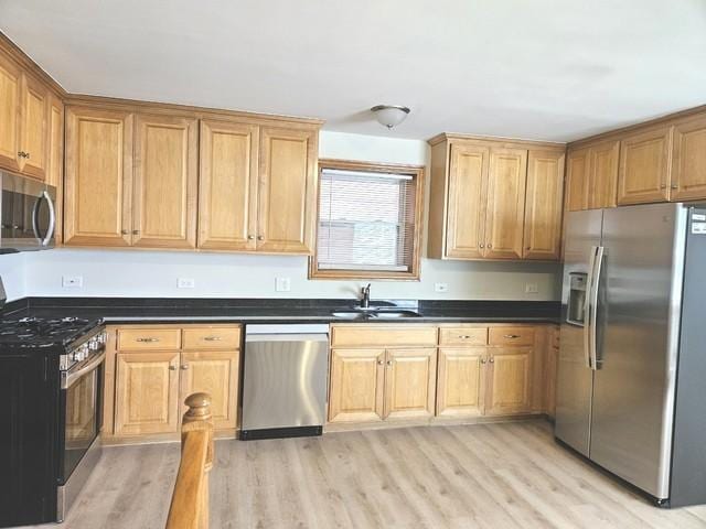 kitchen with appliances with stainless steel finishes, a sink, dark countertops, and light wood finished floors