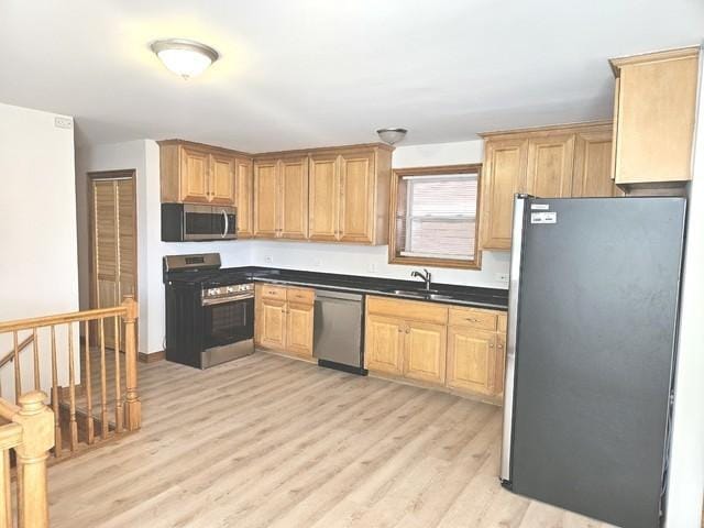 kitchen with appliances with stainless steel finishes, a sink, light wood-type flooring, and dark countertops