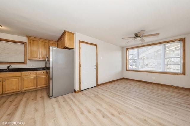 kitchen featuring freestanding refrigerator, light wood-type flooring, dark countertops, ceiling fan, and baseboards