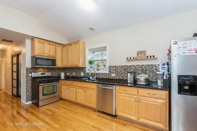 kitchen with stainless steel appliances, a sink, light wood-style flooring, decorative backsplash, and vaulted ceiling