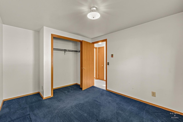 unfurnished bedroom with baseboards, dark colored carpet, and a closet