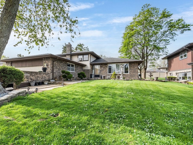 rear view of house featuring a chimney, a lawn, brick siding, and a patio area