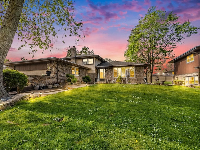 view of front of home featuring a chimney, a lawn, and brick siding