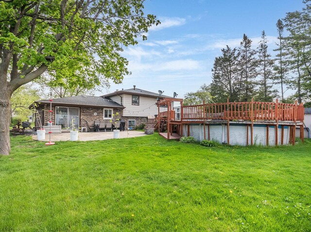view of grassy yard featuring a deck, a patio area, stairway, and an outdoor pool