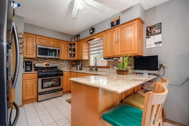 kitchen featuring appliances with stainless steel finishes, a sink, a peninsula, tasteful backsplash, and a breakfast bar area