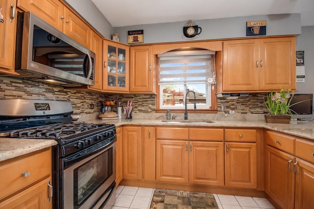 kitchen featuring appliances with stainless steel finishes, a sink, light stone countertops, decorative backsplash, and light tile patterned floors