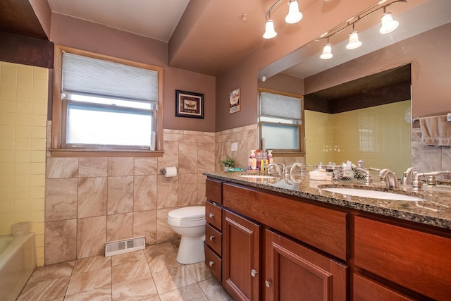 full bath featuring tile walls, toilet, double vanity, and wainscoting