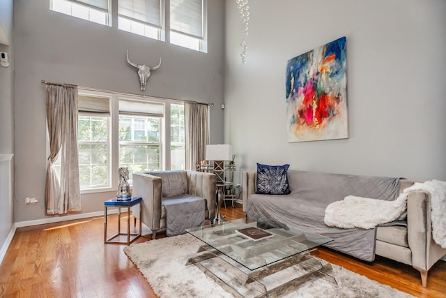 living area with healthy amount of natural light, a towering ceiling, wood finished floors, and baseboards