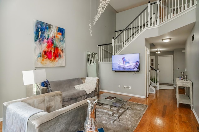 living area with stairs, baseboards, wood finished floors, and a high ceiling