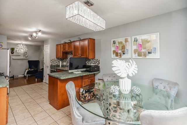 kitchen featuring brown cabinets, decorative backsplash, a peninsula, light tile patterned flooring, and freestanding refrigerator