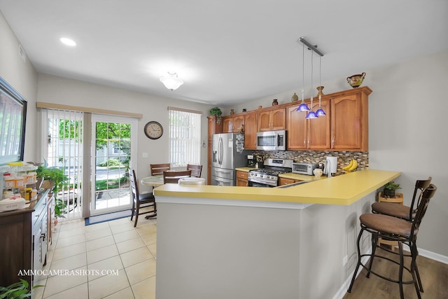 1677 Brightwood Pl Unit 8B, Aurora, IL 60506 - kitchen featuring appliances with stainless steel finishes, brown cabinetry, a peninsula, light countertops, and decorative backsplash