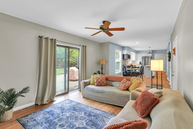 living area featuring a ceiling fan, baseboards, and light wood-style flooring