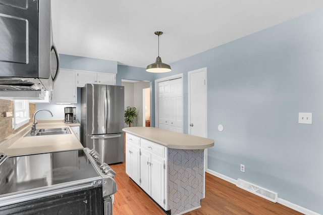 kitchen with appliances with stainless steel finishes, a sink, light wood finished floors, and light countertops