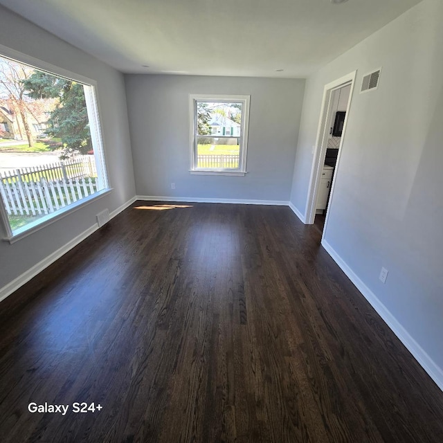 unfurnished room featuring healthy amount of natural light, dark wood finished floors, and baseboards
