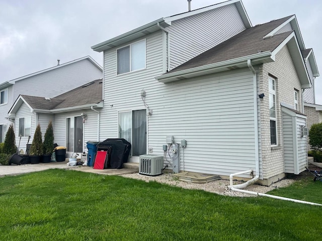 rear view of house with central AC unit, a yard, and roof with shingles