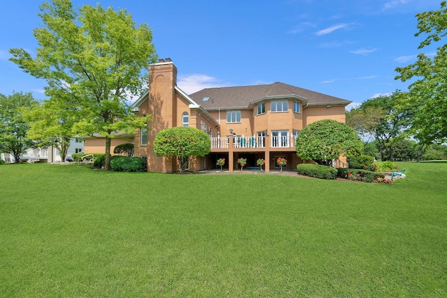 back of property featuring a deck, a lawn, a chimney, and stucco siding