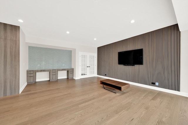 unfurnished living room featuring wood finished floors, an accent wall, french doors, recessed lighting, and baseboards