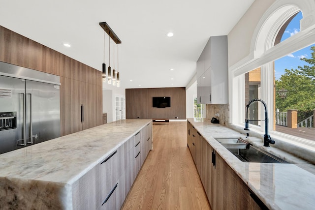 kitchen featuring modern cabinets, stainless steel built in fridge, a sink, light wood finished floors, and light stone counters