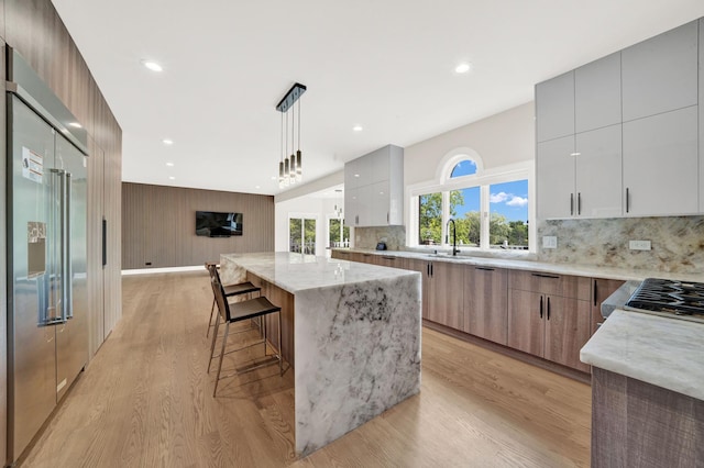 kitchen featuring modern cabinets, high end fridge, light wood-style floors, light stone counters, and a sink