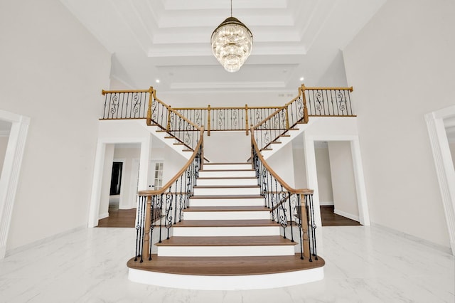 staircase with a chandelier, marble tiled flooring, a raised ceiling, a towering ceiling, and baseboards