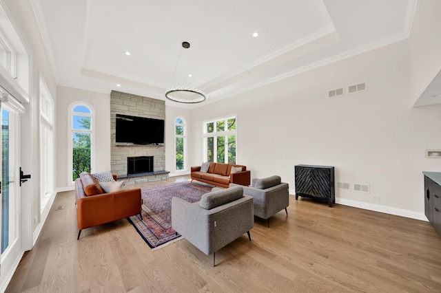 living area featuring a tray ceiling, light wood-type flooring, a fireplace, baseboards, and recessed lighting