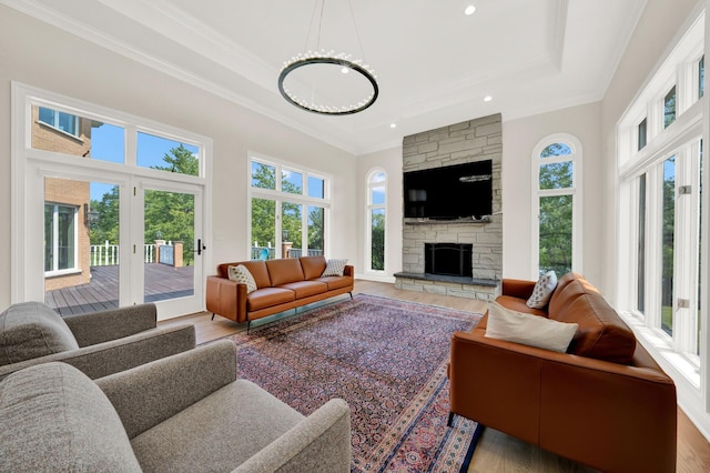 living area with crown molding, wood finished floors, a tray ceiling, a stone fireplace, and recessed lighting