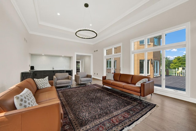 living room featuring a tray ceiling, wood finished floors, crown molding, baseboards, and a chandelier