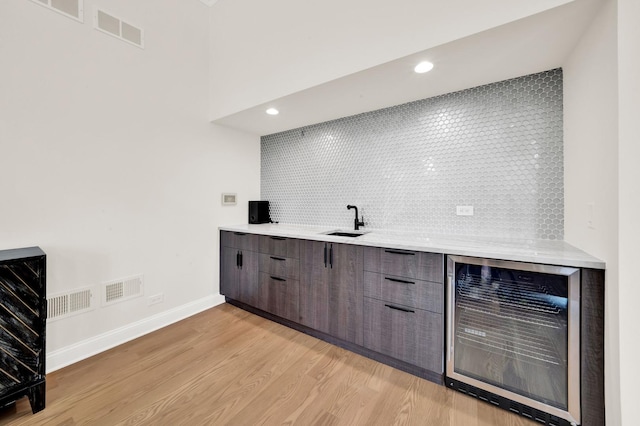 indoor bar featuring beverage cooler, light wood-style flooring, backsplash, baseboards, and recessed lighting