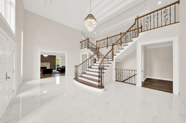 foyer entrance with a high ceiling, a chandelier, marble tiled flooring, stairs, and a premium fireplace