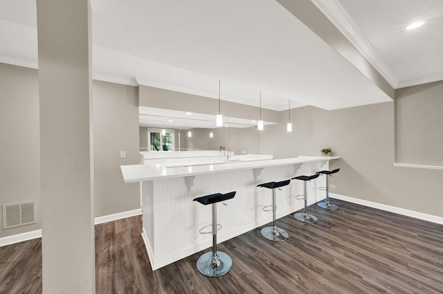 kitchen featuring baseboards, crown molding, dark wood-style flooring, a kitchen breakfast bar, and light countertops