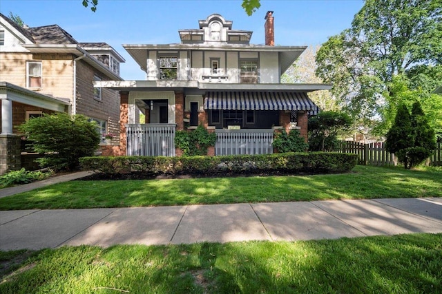 american foursquare style home featuring a chimney, a porch, brick siding, and a balcony